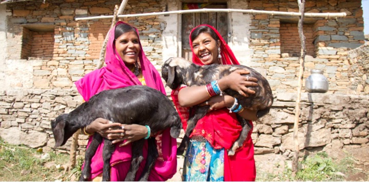 two women holding goats outside